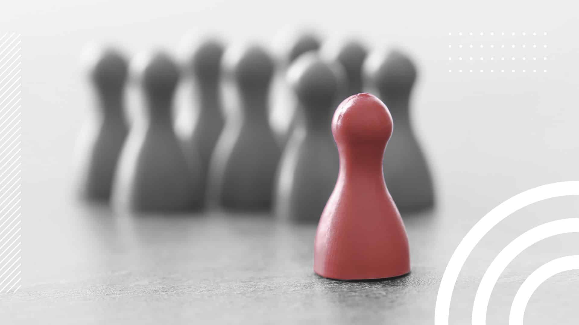 a group of pawn pieces blurred in the background behind a singular red pawn, a metaphor for discrimination