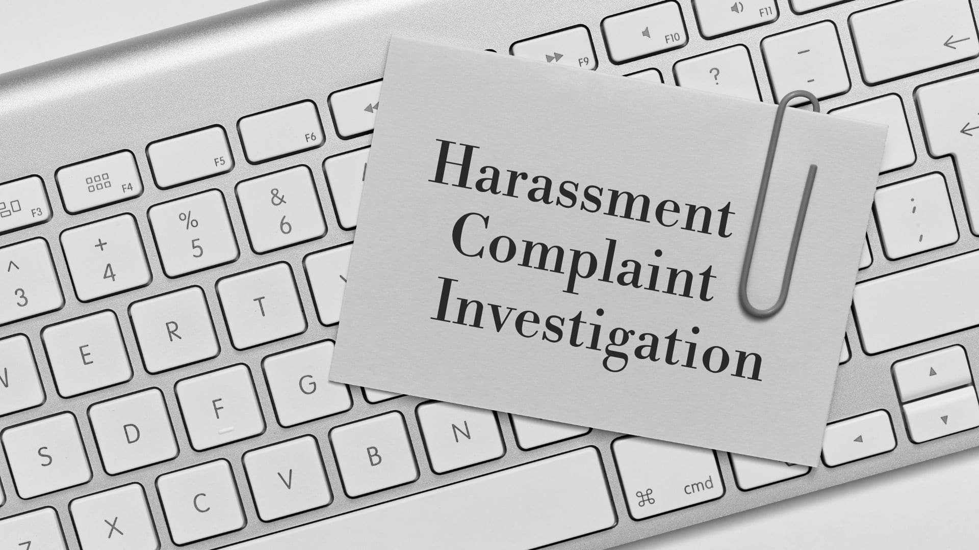 a notecard that reads "harassment complaint investigation" with a paperclip on it resting on a computer keyboard