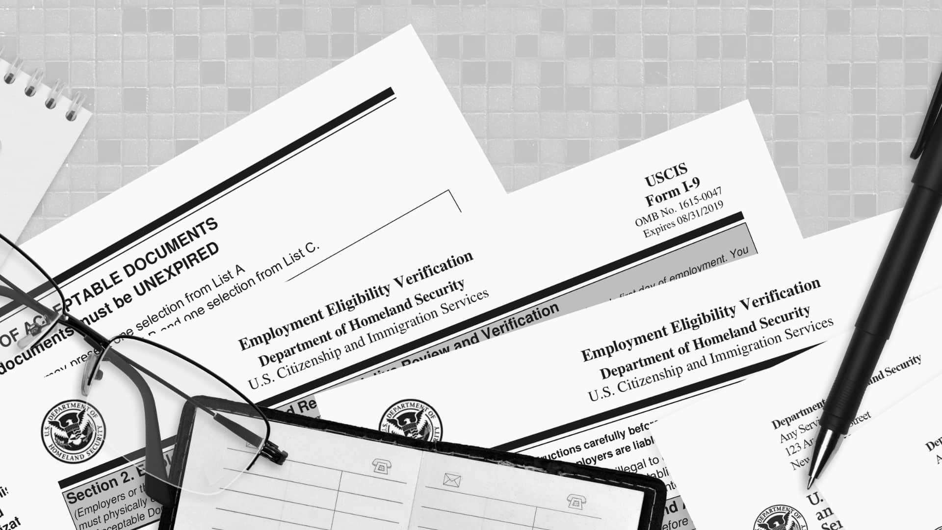 various immigration documents, a pen, and a pair of glasses laid out on a desk in close-up