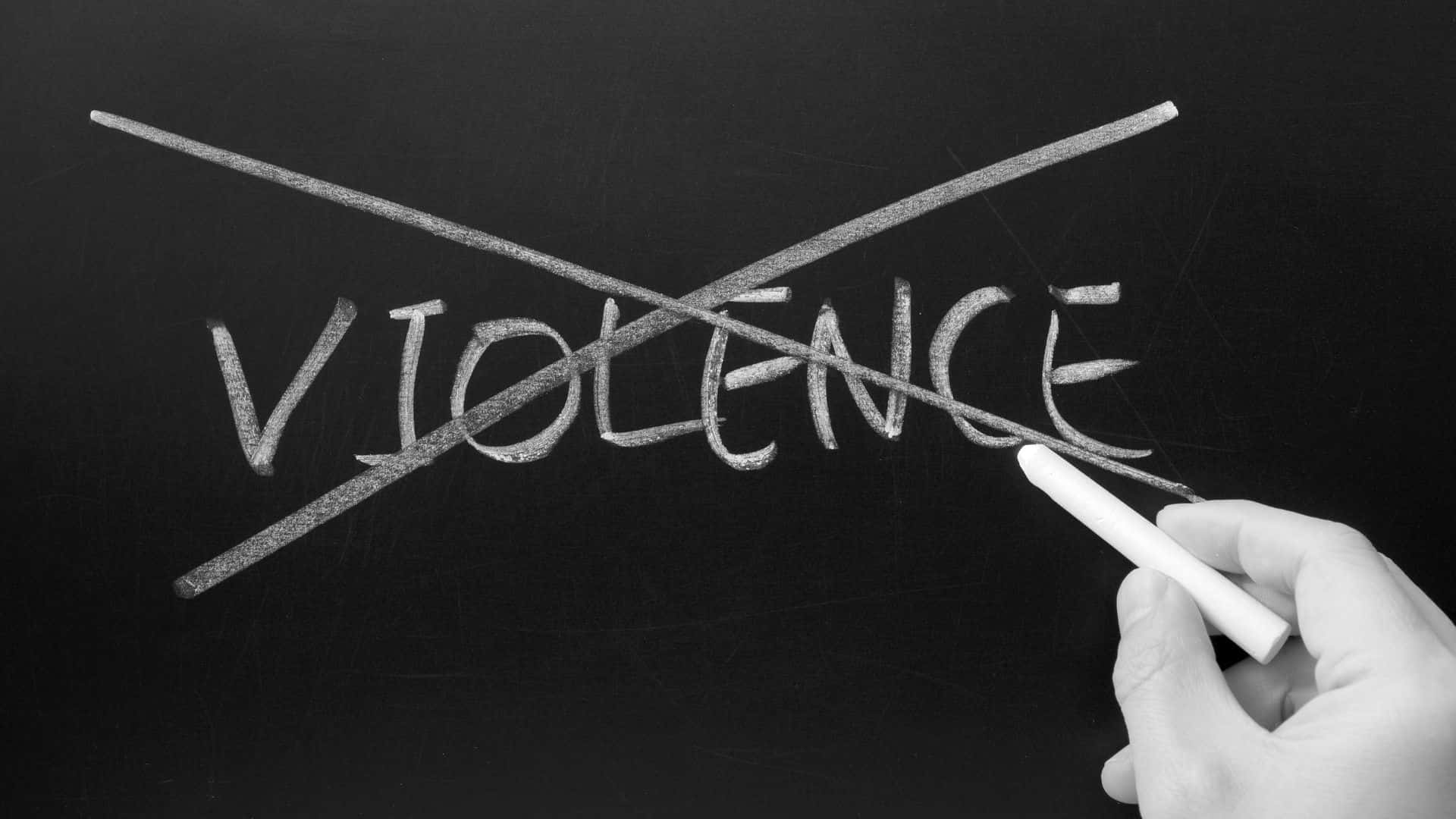 hand crossing out the word "violence" on a chalkboard with a piece of chalk