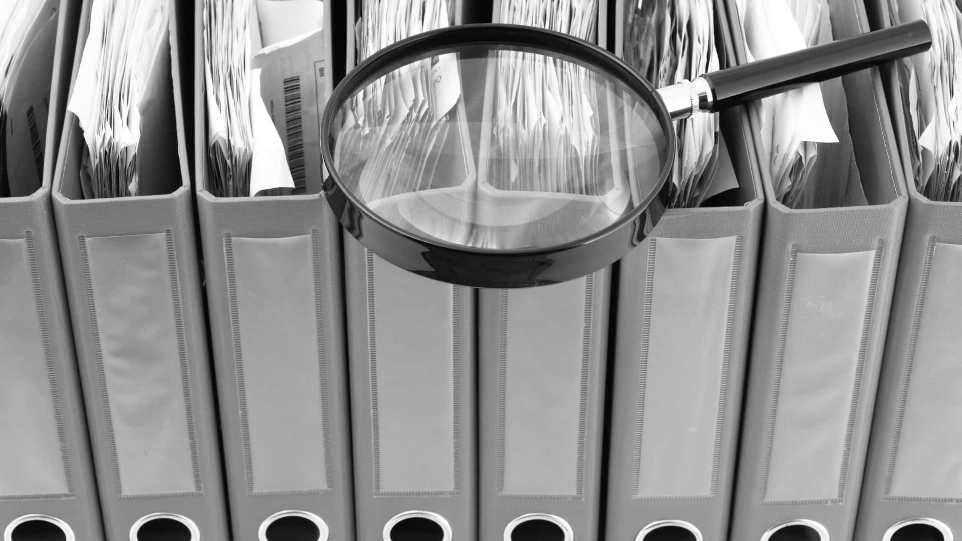 Many binders stood up with a magnifying glass balanced at the edge of their spines