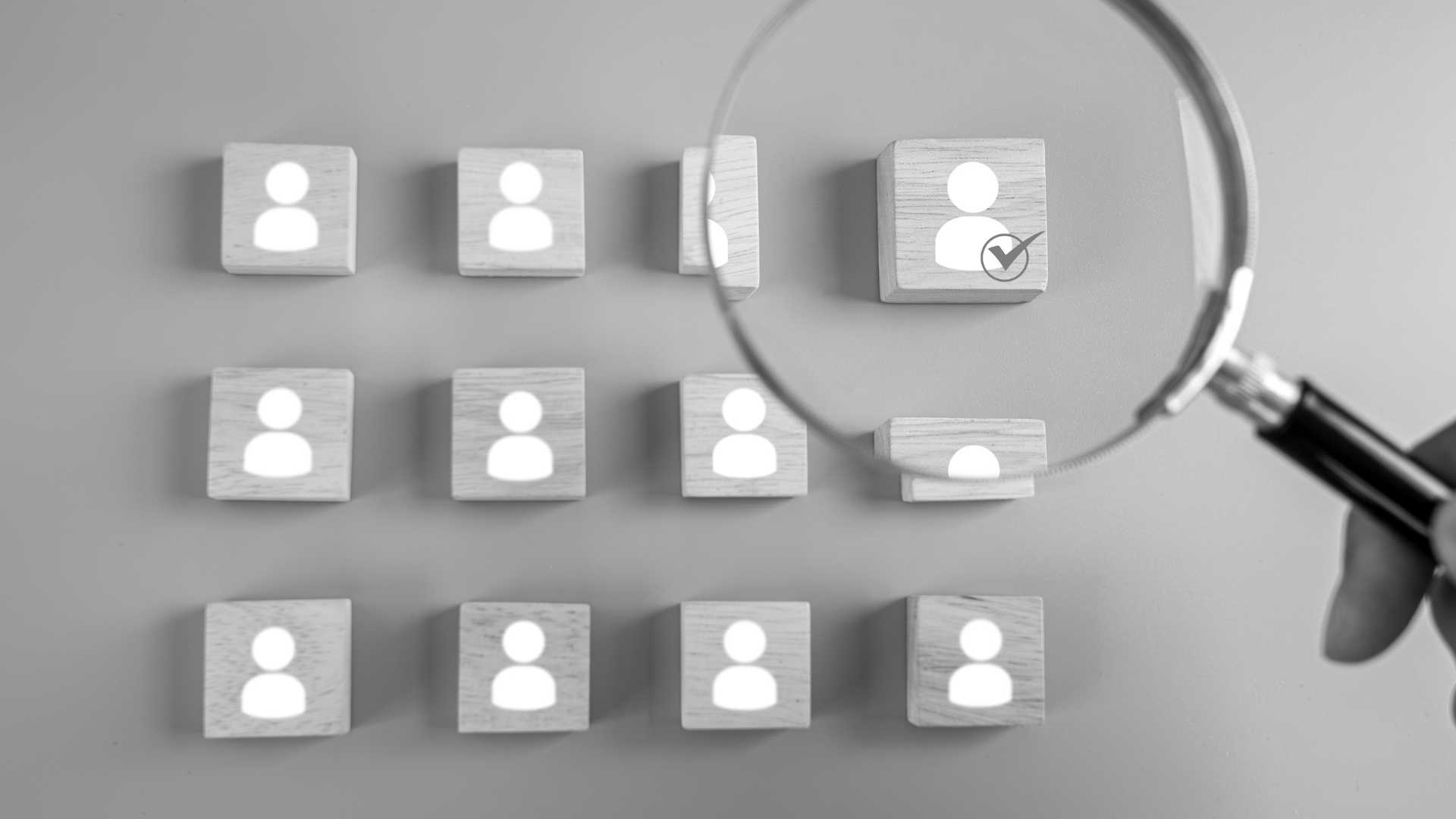 small wooden cubes with user icons printed on each, over the top rightmost cube, a hand holds a magnifying glass over it.