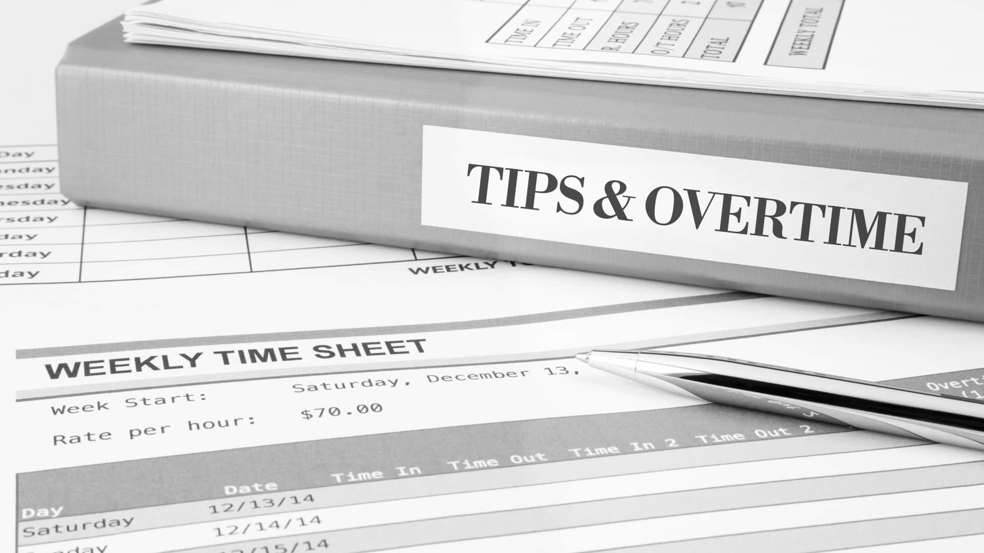 binder sitting on time sheets, on the spine of the binder is "TIPS & OVERTIME"